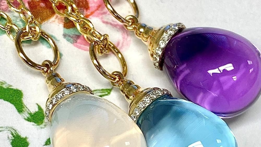 Three different color gemstones shaped like tear drops on yellow gold chains with diamonds